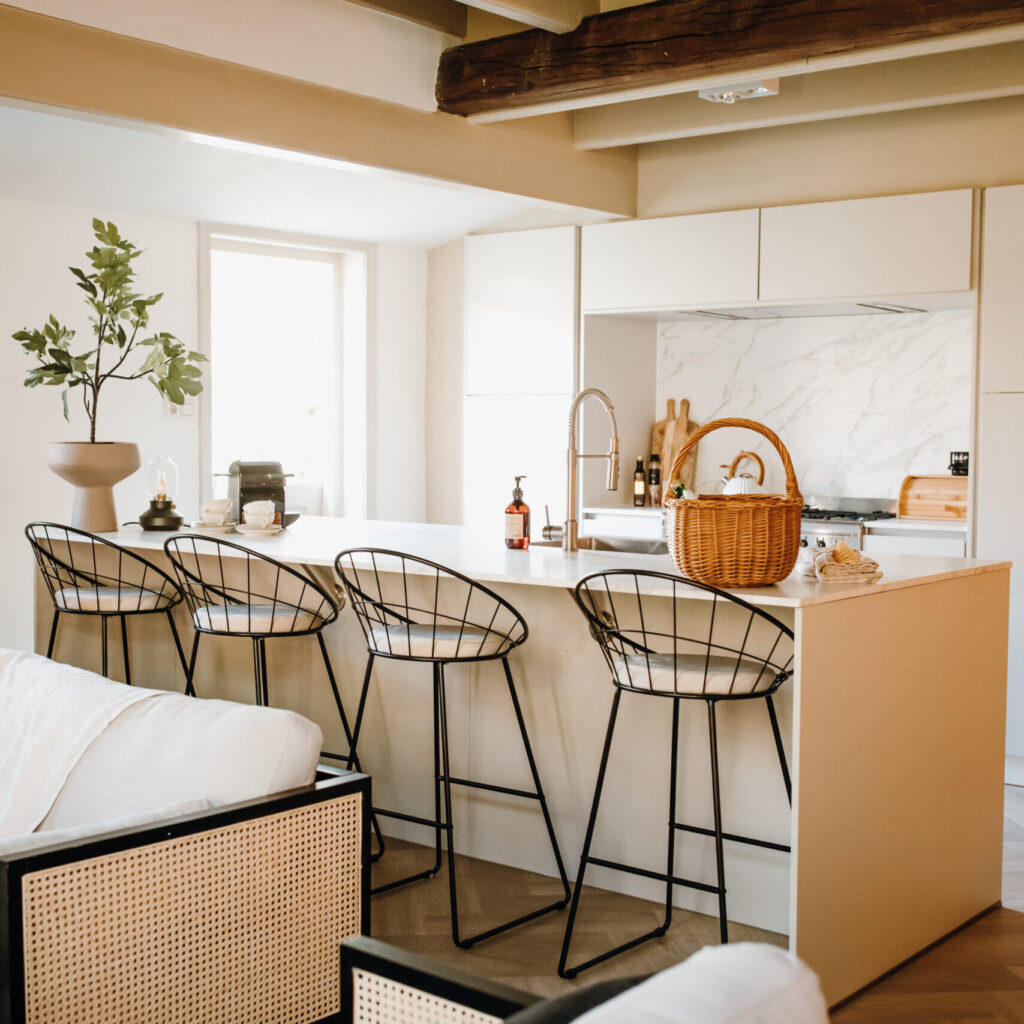 Foto van een inrichting met een kookeiland, krukken en bank in neutrale tinten